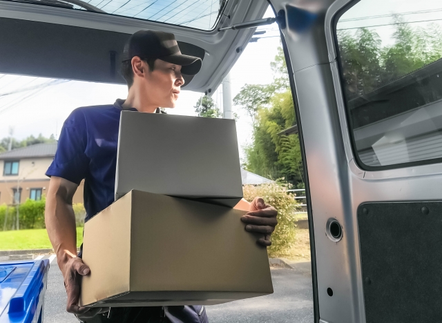 軽バンから段ボール荷物を取り出す配達員